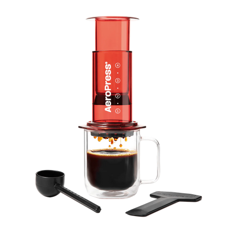 AeroPress coffee maker with a glass mug of coffee and scoop on a white background #color_red