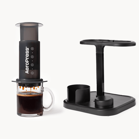 Aeropress coffee maker with a glass of brewed coffee on a white background