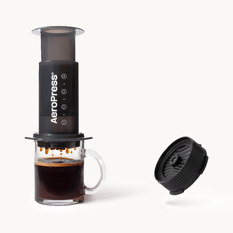 Aeropress coffee maker with a glass of brewed coffee on a white background