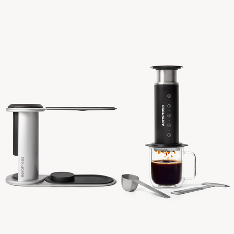 AeroPress coffee maker with a glass of coffee and accessories on a white background #color_black