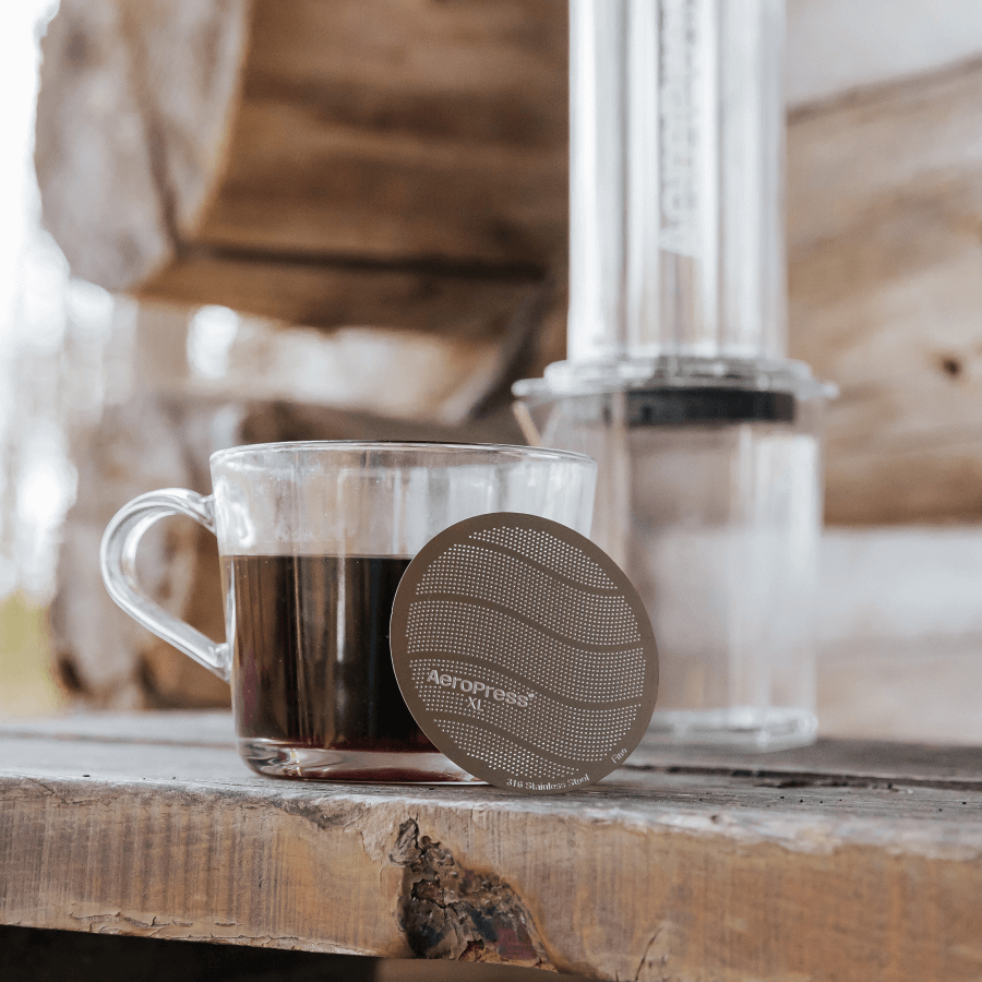 Clear glass mug with coffee and Aeropress filter on a wooden surface