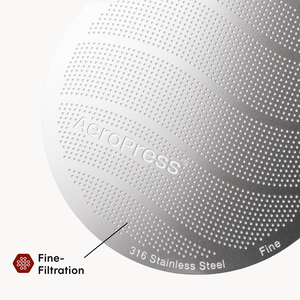 Close-up of an AeroPress coffee maker with 'AeroPress' branding and text indicating 316 stainless steel and fine filtration. #color_pink