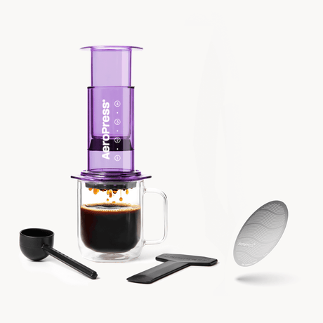 Purple AeroPress coffee maker with a glass mug, scoop, and filter on a white background #color_purple