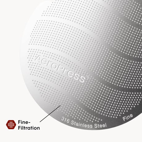 Close-up of an AeroPress coffee maker with 'AeroPress' branding and text indicating 316 stainless steel and fine filtration.  #color_purple