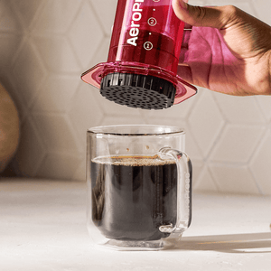 Person using an Aeropress to make coffee in a clear mug. #color_pink