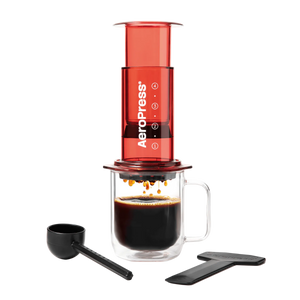 AeroPress coffee maker with a glass mug of coffee and scoop on a white background #color_red