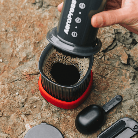 A person using an AeroPress Go Travel coffee maker on a stone surface