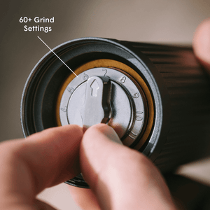 Hand adjusting  AeroPress manual coffee grinder with '60+ Grind Settings' text.