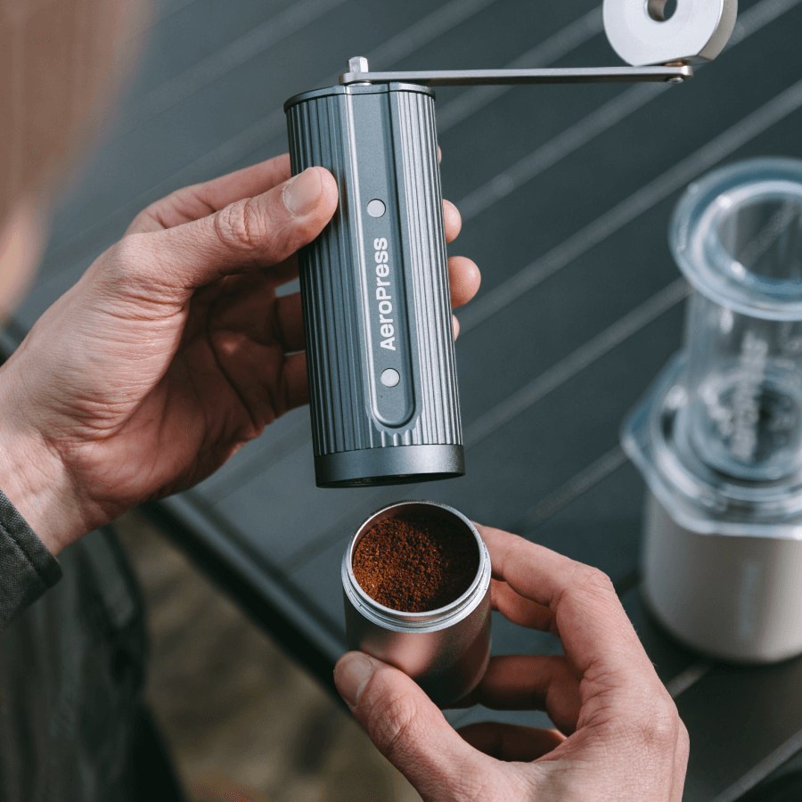 Person using an AeroPress manual coffee grinder with a focus on the coffee grounds.