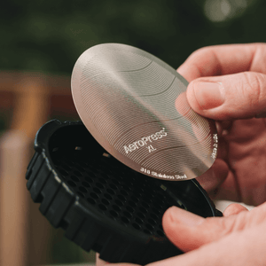 Person holding a black AeroPress coffee maker with a silver filter.