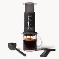 AeroPress Original coffee maker with a glass of brewed coffee on a white background