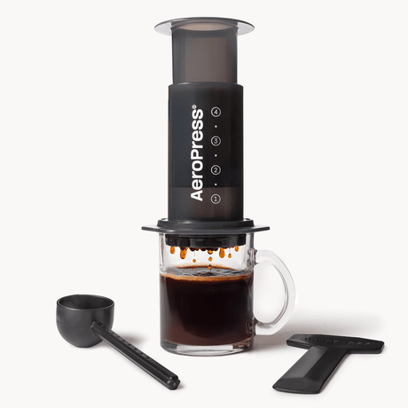 AeroPress Original coffee maker with a glass of brewed coffee on a white background