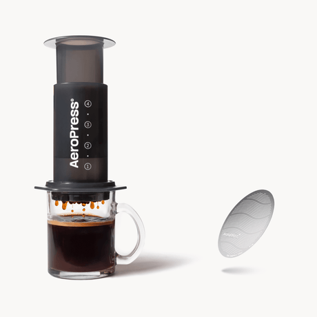 Aeropress coffee maker with a glass of coffee and filter on a white background