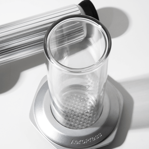 Clear glass AeroPress Premium chamber with metal base on a white  surface #color_silver