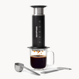 AeroPress Steel coffee maker with a glass mug of coffee on a white background #color_black