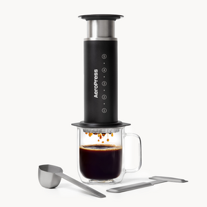 AeroPress Steel coffee maker with a glass mug of coffee on a white background #color_black
