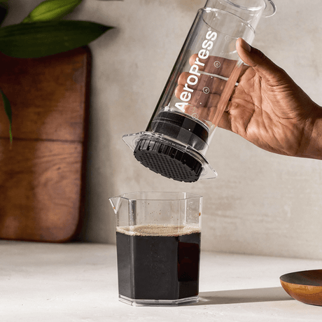 A person using an Aeropress to make coffee on a countertop.